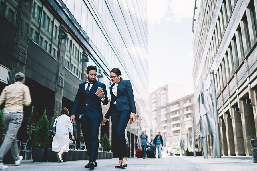 Contact - Two Business People Walking Down Street in the City Looking at a Phone